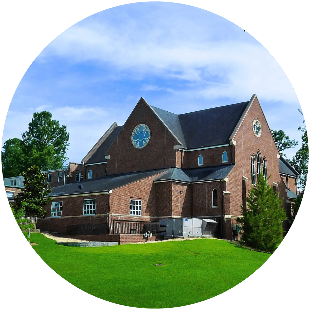 Red-brick Episcopal church with large stained-glass windows, steep roof, and lush green lawn under a blue sky.