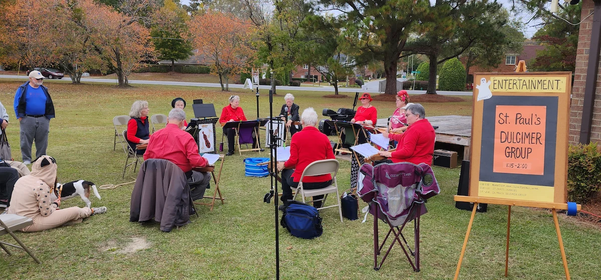 dulcimers_624 St. Paul's Dulcimer Group playing outdoors near an Episcopal church sign. Audience includes people seated and a dog on the grass.